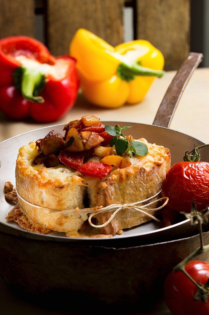 Gratinated baguette stuffed with a pepper medley in a pan with braised cocktail tomatoes