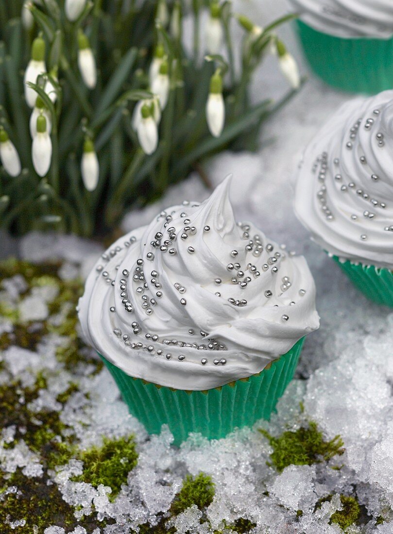 Cupcakes decorated with white frosting and silver pearls in fake snow