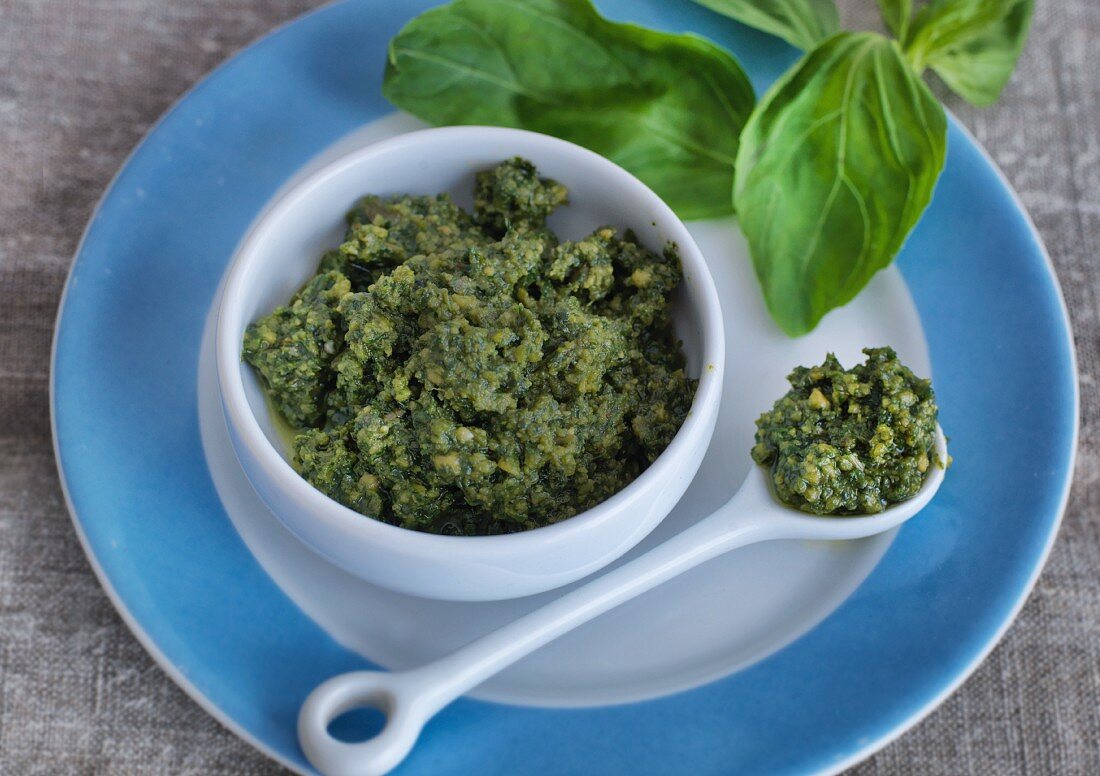 Basil pesto in a bowl and a porcelain spoon