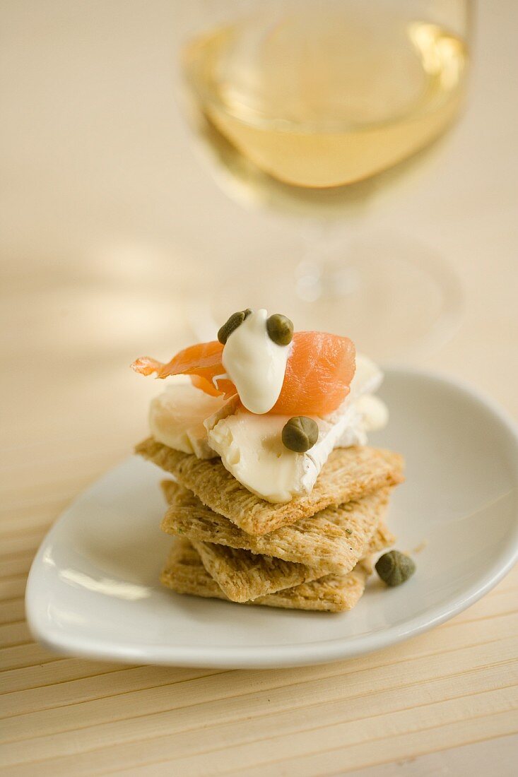 A stack of crackers topped with soft cheese, salmon and capers served with white wine