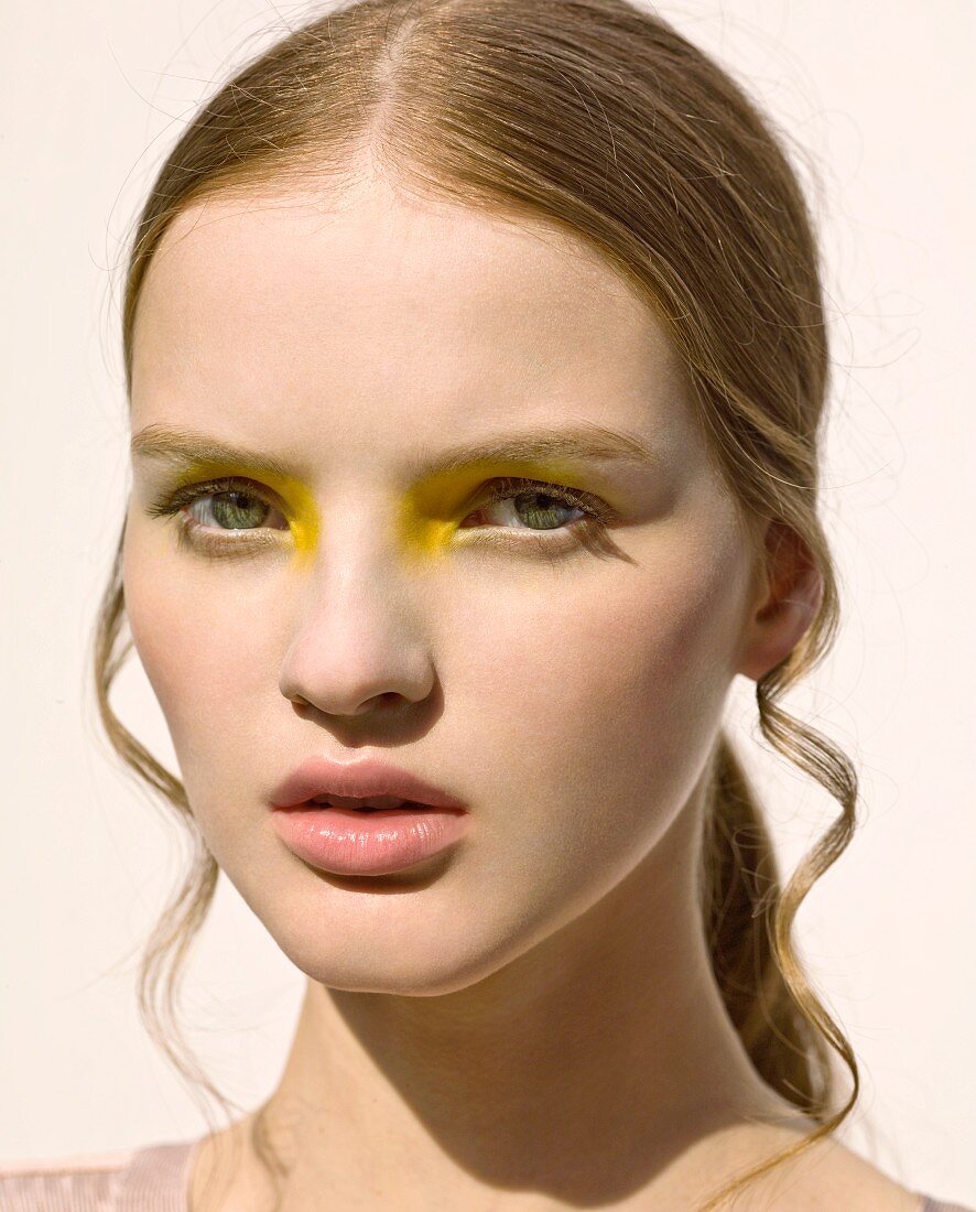 A close-up portrait of a young woman wearing yellow eyeshadow