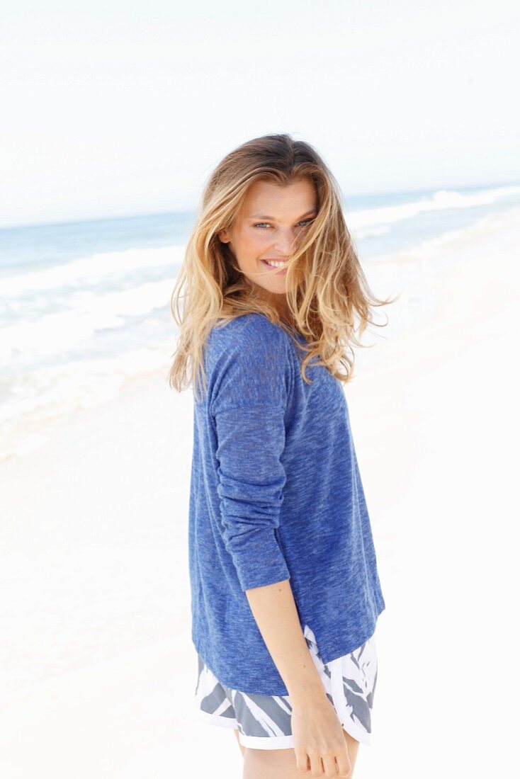 A young woman on a beach wearing a blue flecked jumper