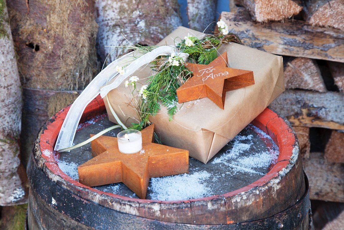 Verpacktes Weihnachtsgeschenk mit beschriftetem Holzstern auf verschneitem Fass