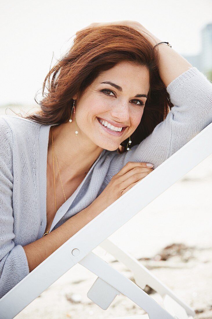 A brunette woman sitting on a deck chair wearing grey cardigan