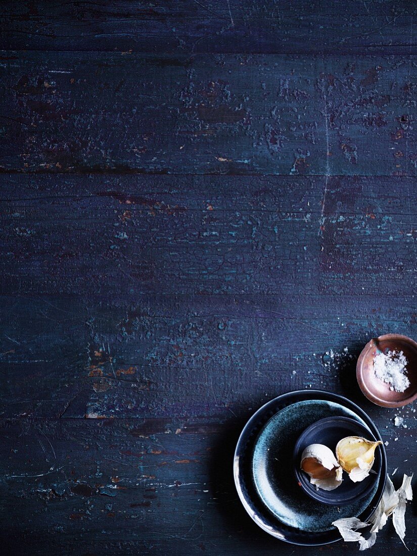 Blaue Holzfläche mit Knoblauchzehen und Salz in Schälchen