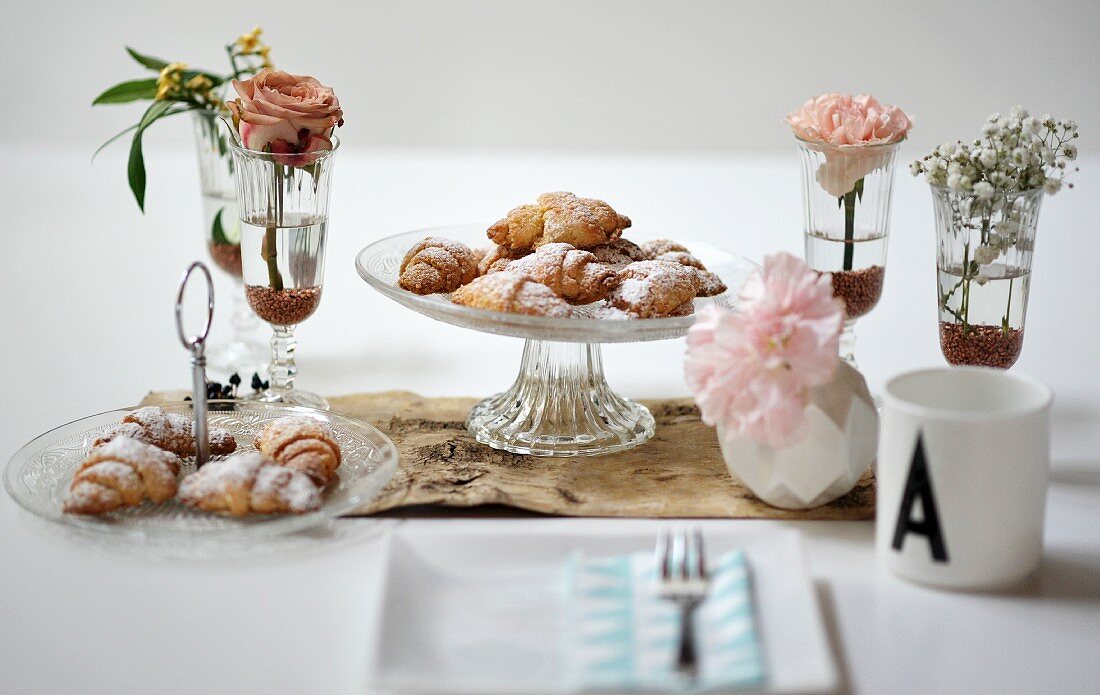 Croissants with icing sugar on a cake stand between vases of flowers