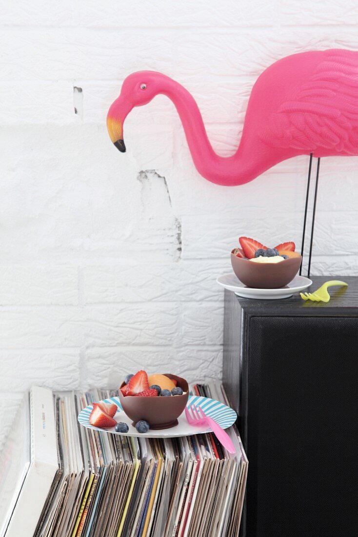 Mit Luftballons gestaltete Schokoladenschalen mit Früchten als essbares Partygeschirr und dekorative Flamingofigur auf Lautsprecherbox