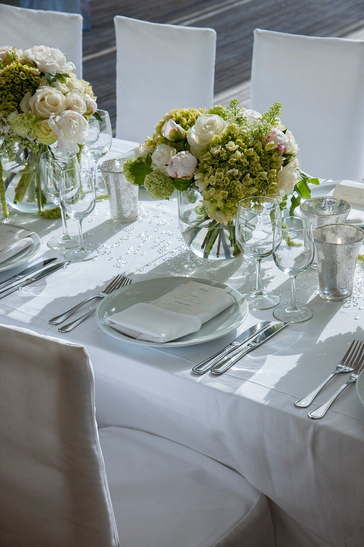 Bouquets of white roses on festively set wedding dinner table with white tablecloth