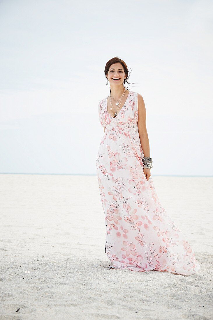 A brunette woman on a beach wearing a long summer dress