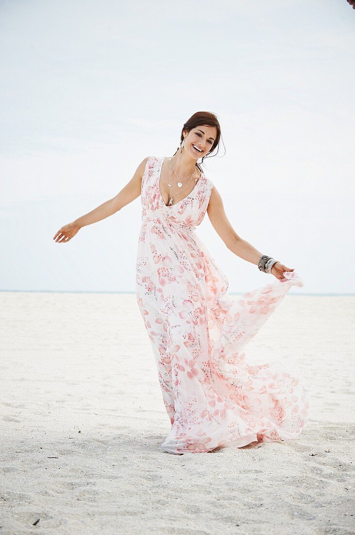 A brunette woman on a beach wearing a long summer dress