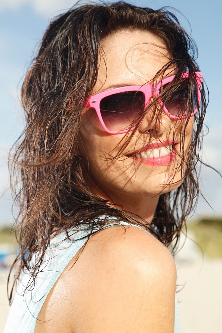 A brunette woman on a beach with damp hair and sunglasses