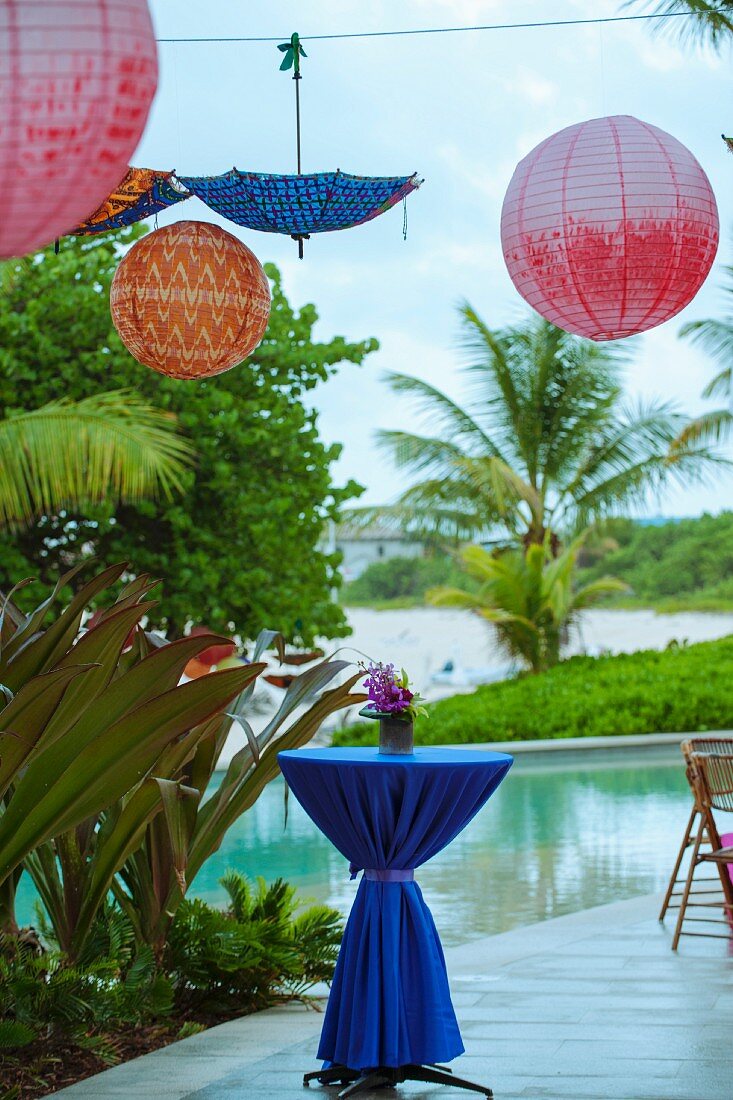 Stehtisch mit drapiertem, dunkelblauem Tischtuch auf festlich dekorierter Terrasse, oberhalb auf Seil gehängte Ballons und Schirm