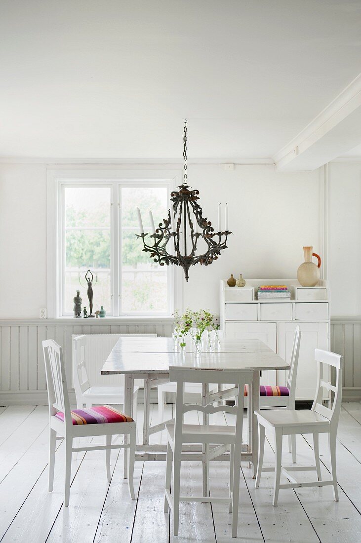 Weisser Tisch mit Holzstühlen unter Kronleuchter in ländlichem Ambiente mit weißem Dielenboden
