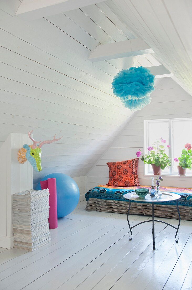 White, wood-clad attic room with side table in front of comfortable daybed below window