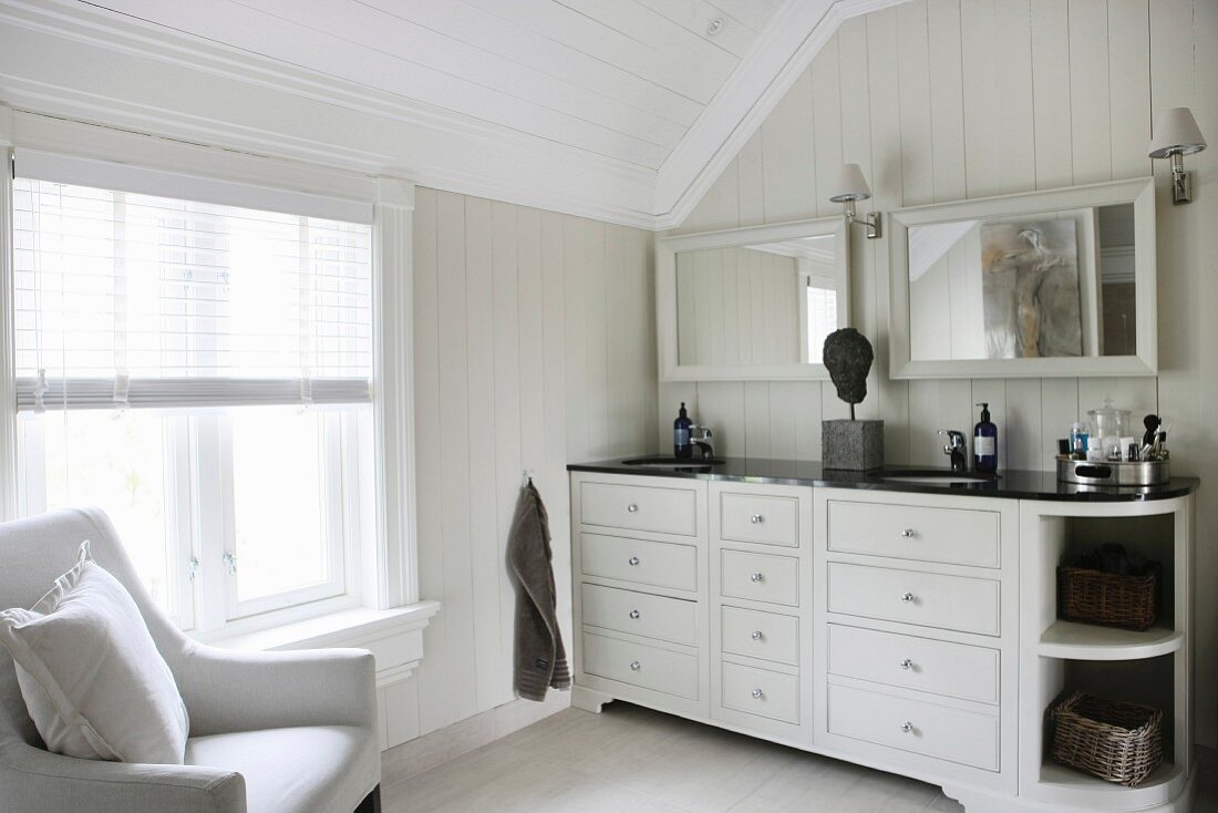 Washstand with twin sinks and armchair in elegant attic bathroom