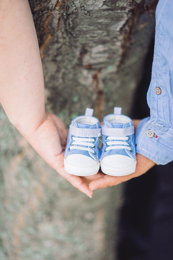 Paar hält Händchen und blau-weiße Babyschuhe