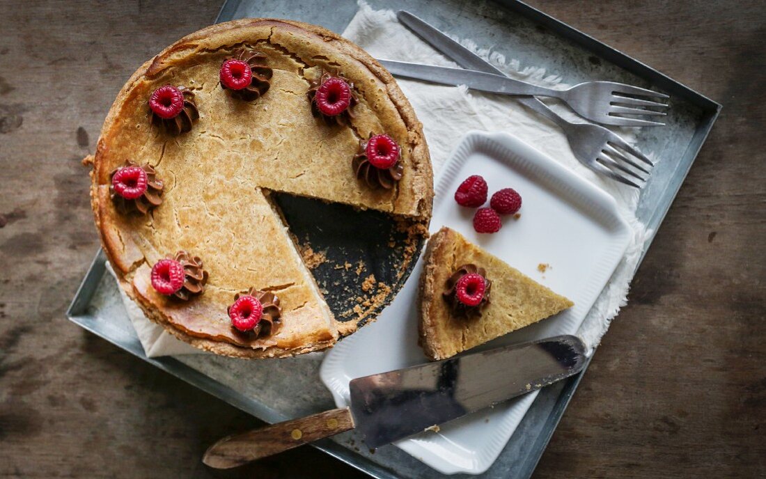 Veganer Käsekuchen mit Himbeeren auf Metalltablett und Holztischplatte