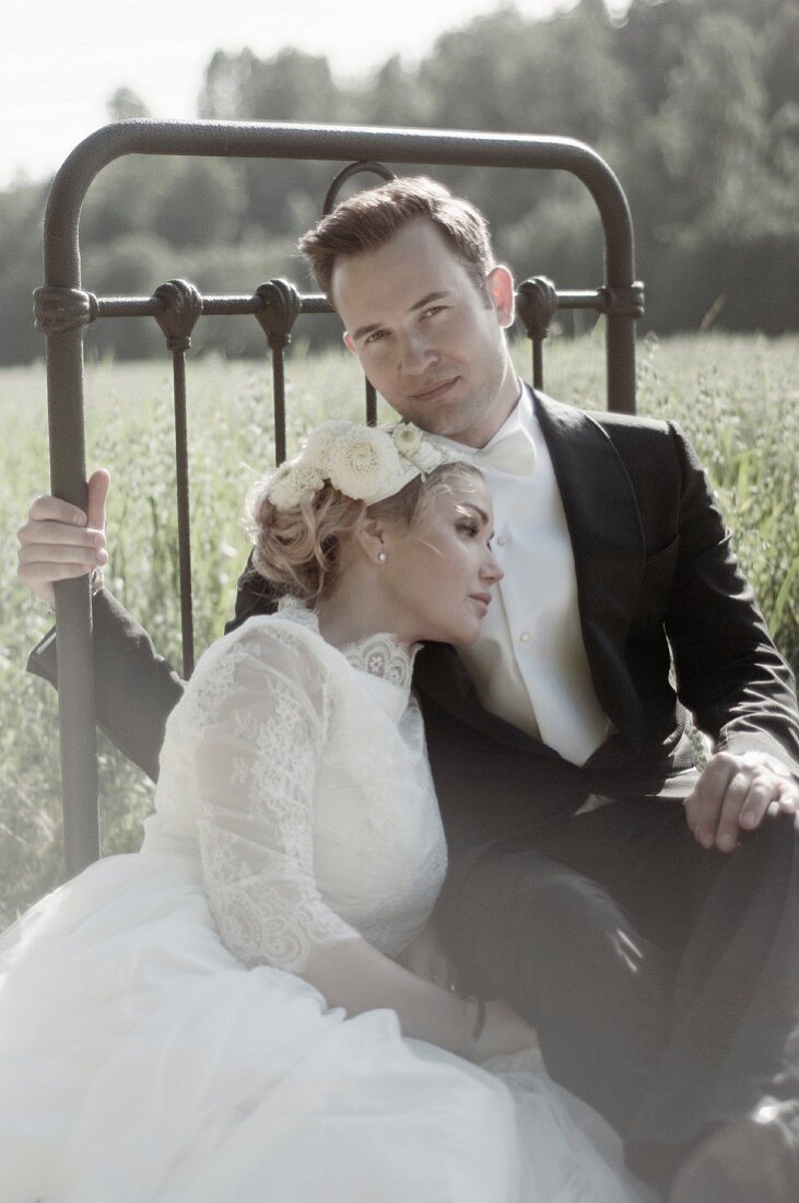 A young bride and groom sitting outside on a bedstead