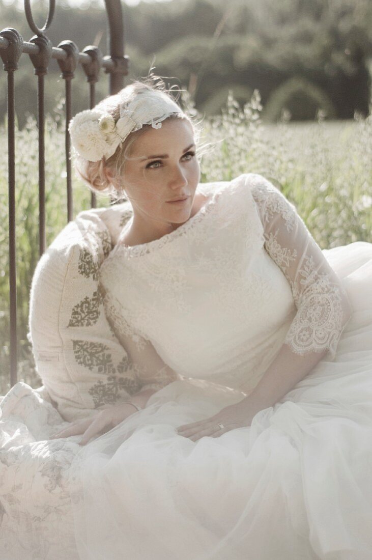 A young bride lying on a metal bedstead outside