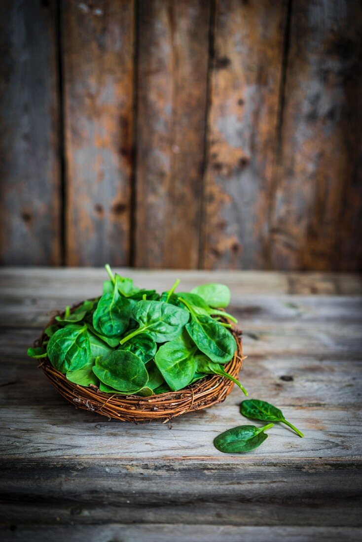 Fresh spinach in a basket on a rustic wooden surface