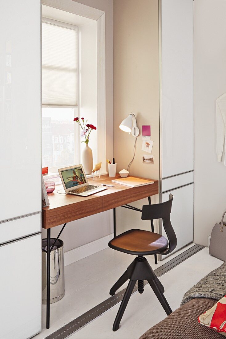 A wooden swivel office chair in front of a minimalistic desk by a window
