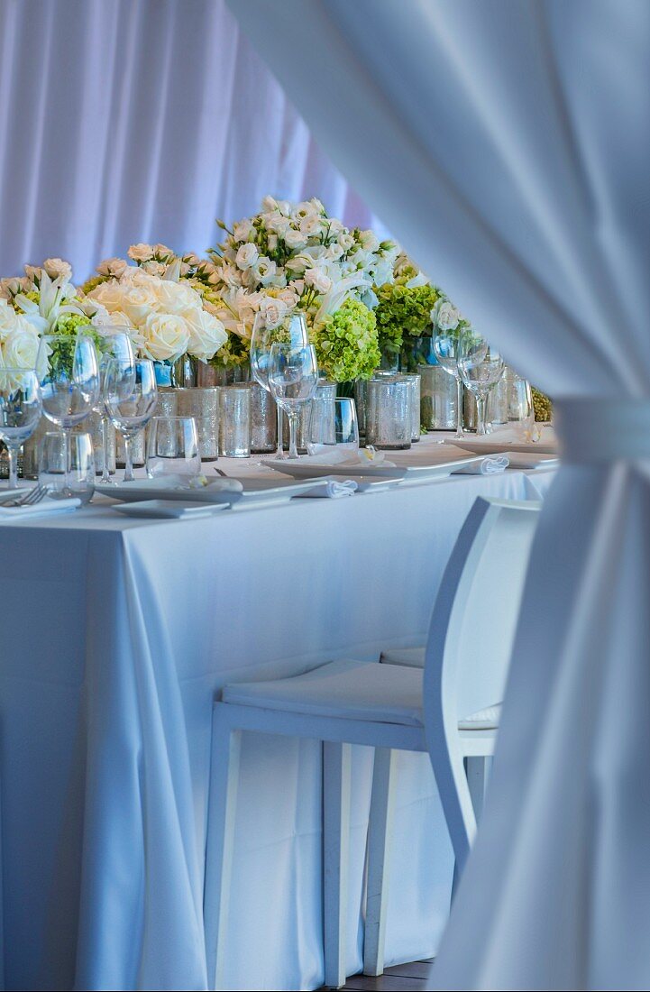 Wedding dinner table festively decorated with row of bouquets and place settings