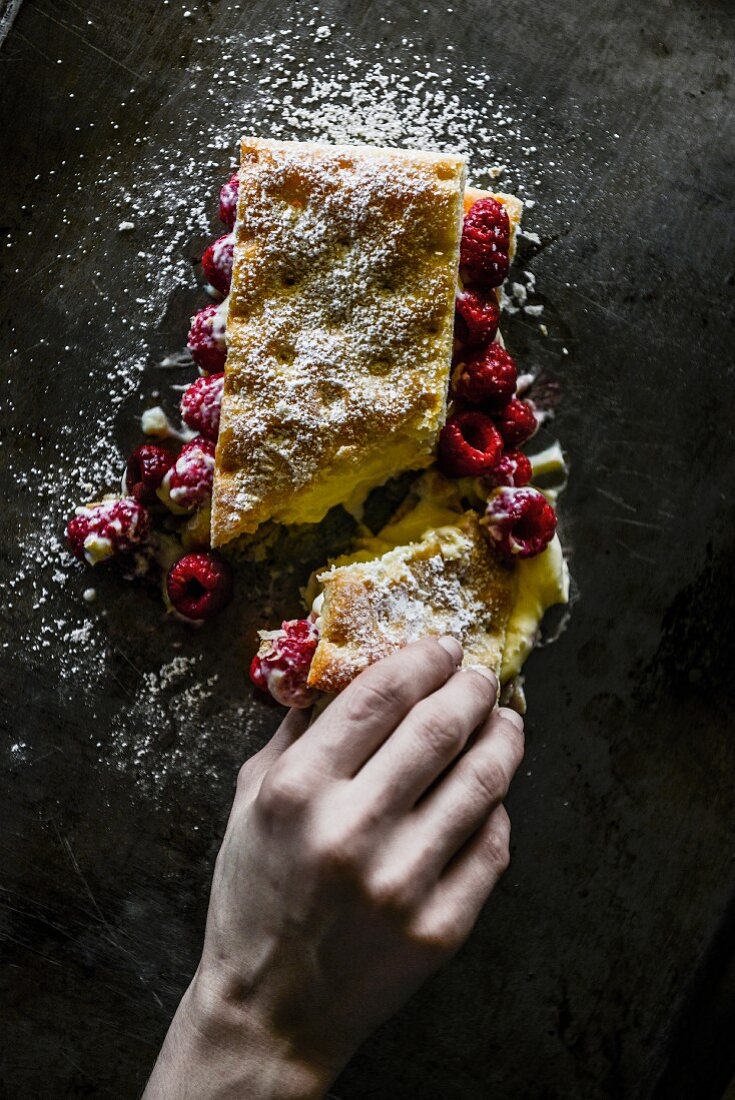 A hand reaching for a slice of raspberry cake