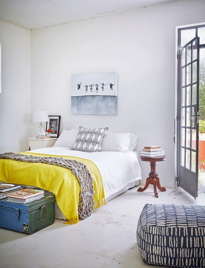 Yellow blanket on double bed, antique bedside table and patterned pouffe in bedroom