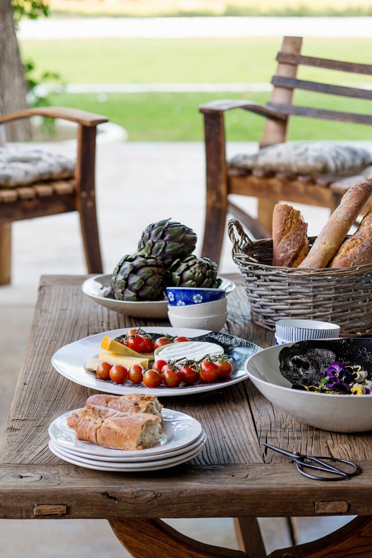 Food in china bowls and basket of bread on rustic table outside