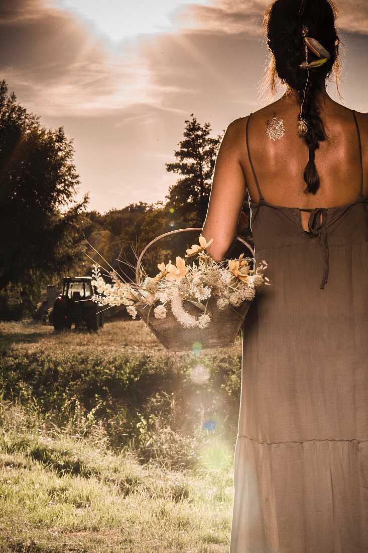 Woman wearing long summer dress and holding basket of flowers in meadow