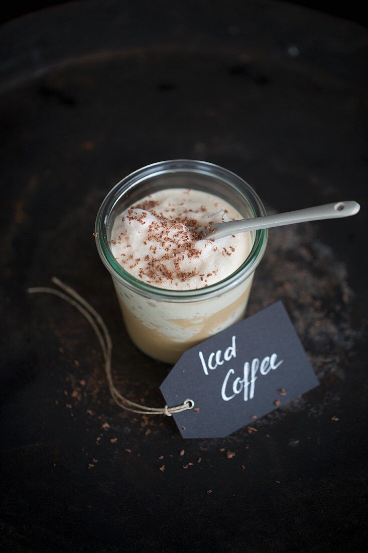 An iced coffee in a jar with a porcelain spoon and a paper label