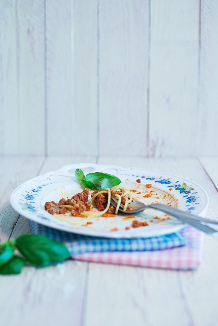The remains of spaghetti Bolognese on a plate with a basil leaf