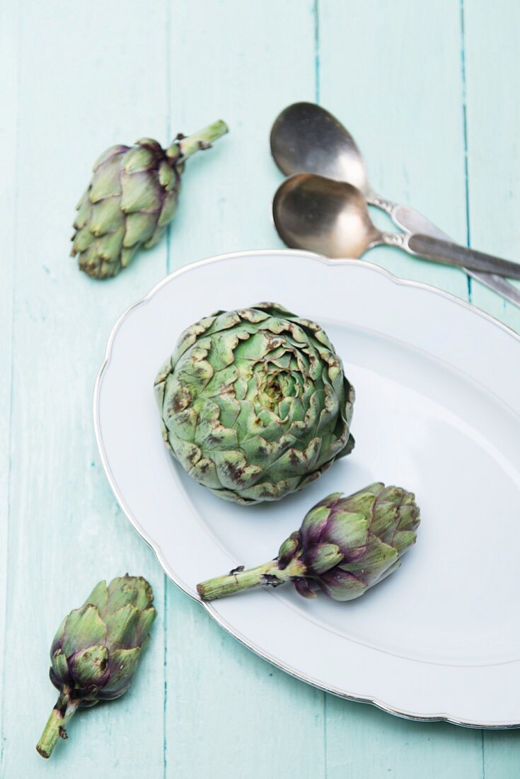 A fresh artichoke and baby artichokes on a porcelain platter