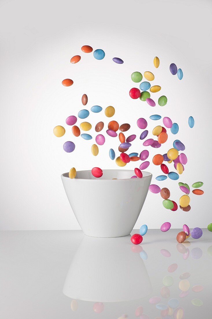 Colourful chocolate beans are flying around a bowl