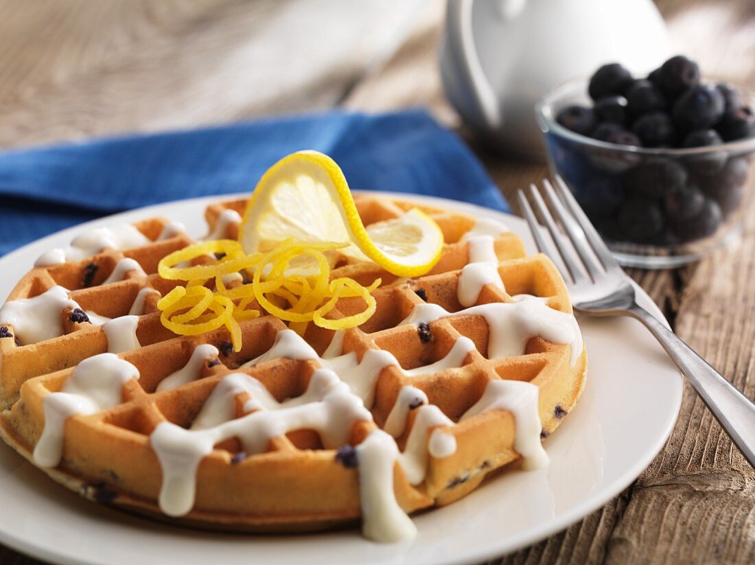A round blueberry waffle with vanilla sauce and lemon zest