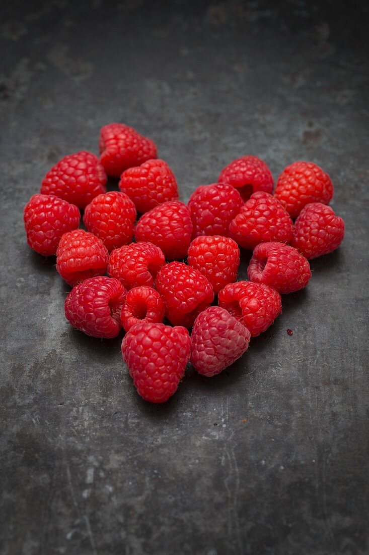 Raspberries arranged in a heart shape on a metal surface