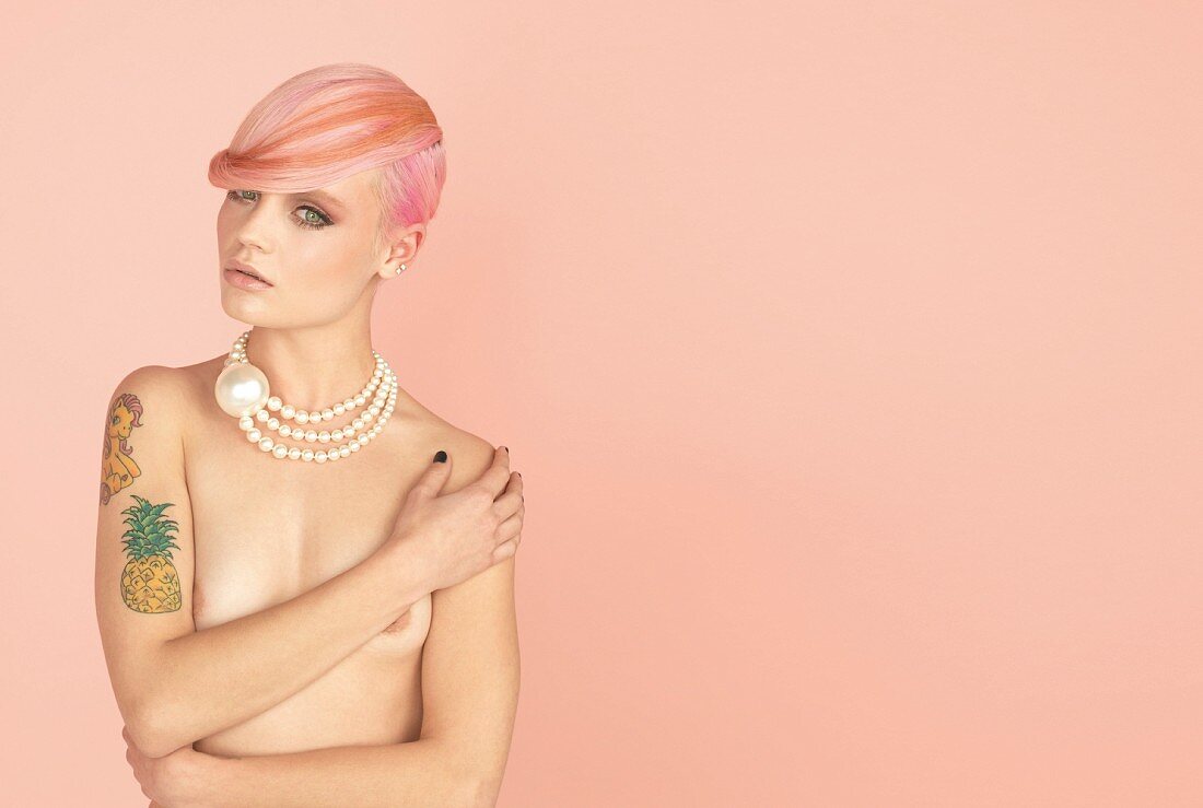 A young woman with pastel pink hair, tattoos and pearl necklace