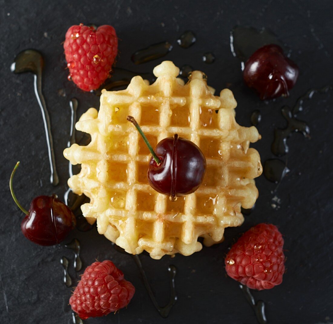 A Belgian waffle with fruit and maple syrup