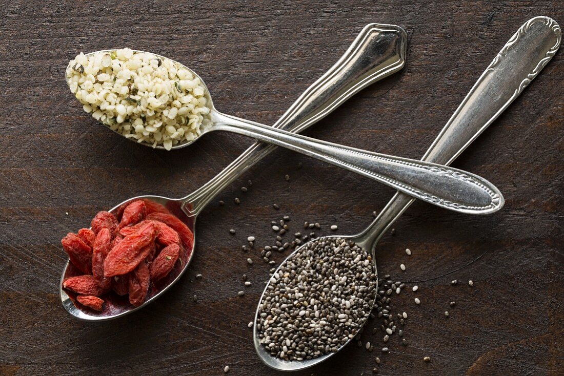 Hemp seeds, chia seeds and goji berries on silver spoons