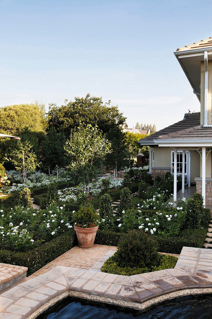 Geometrisch angelegter eleganter Landhaus-Garten mit weißen Blüten und Gartenbrunnen