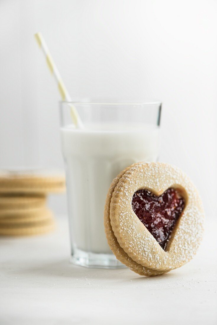 A heart-shaped jam sandwich biscuits in front of a glass of milk