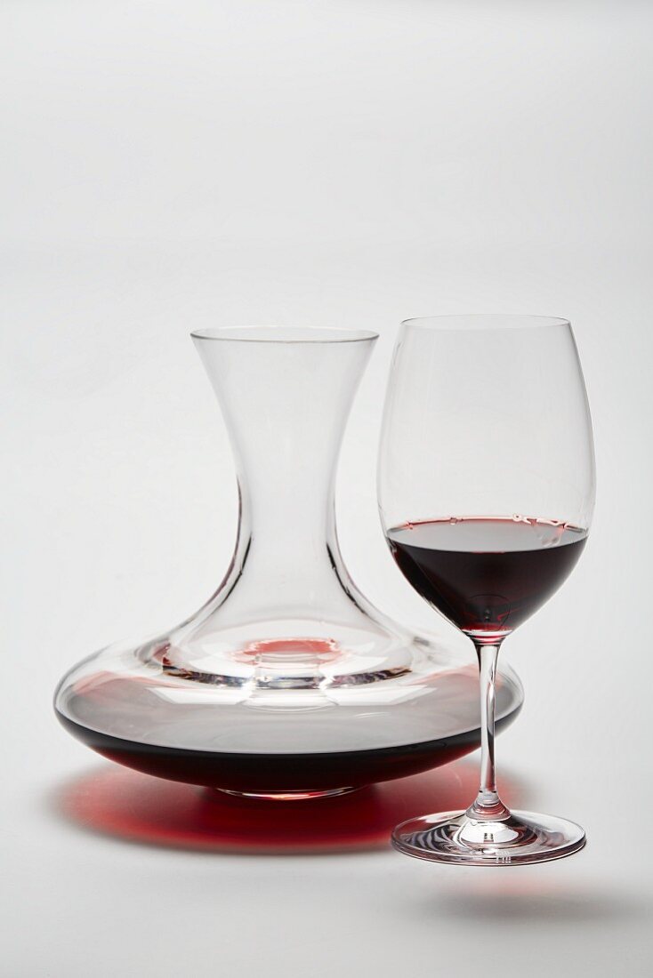 A glass carafe and a glass of red wine on a white surface