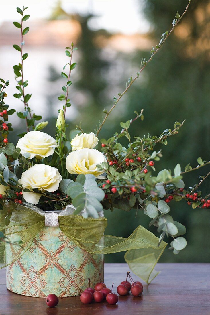 Autumn arrangement of creeping cotoneaster, white eustomas and crab apples in decorated tin