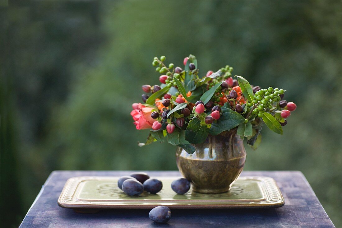 Herbststillleben mit Beerenstrauß in einer Messingvase auf einem Tablett mit Pflaumen