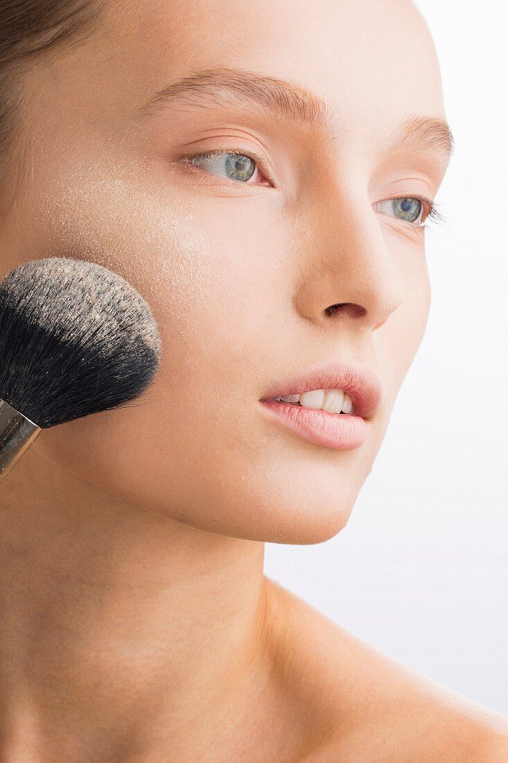 A young woman applying loose powder with a make-up brush