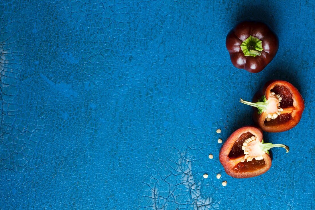 Dark red mini peppers, whole and halved, on a blue surface