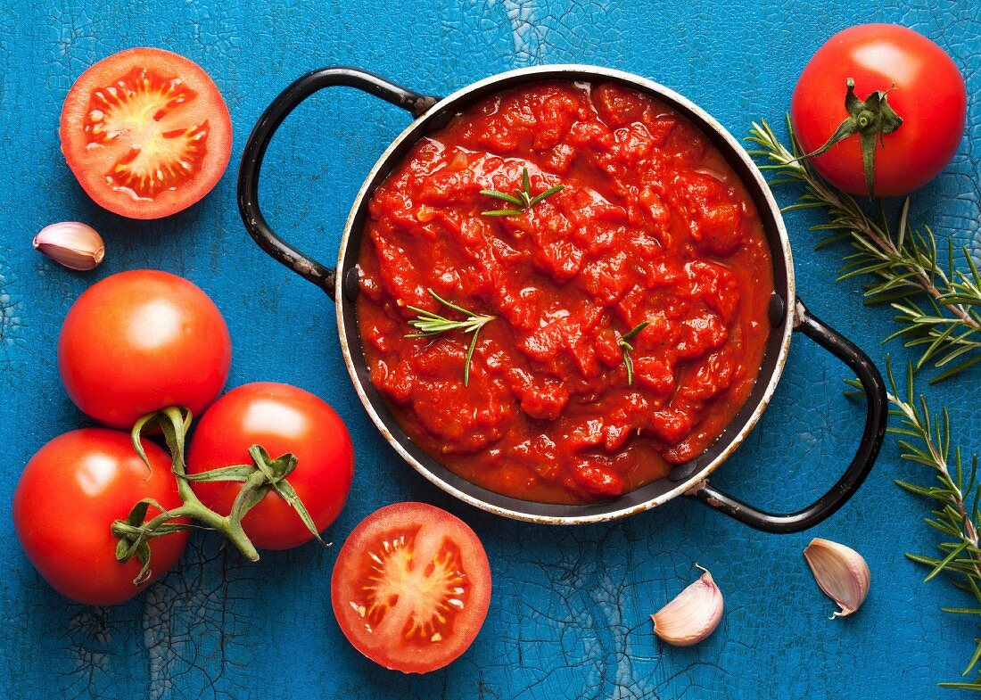 Tomato sauce with rosemary in a pot surrounded by fresh ingredients