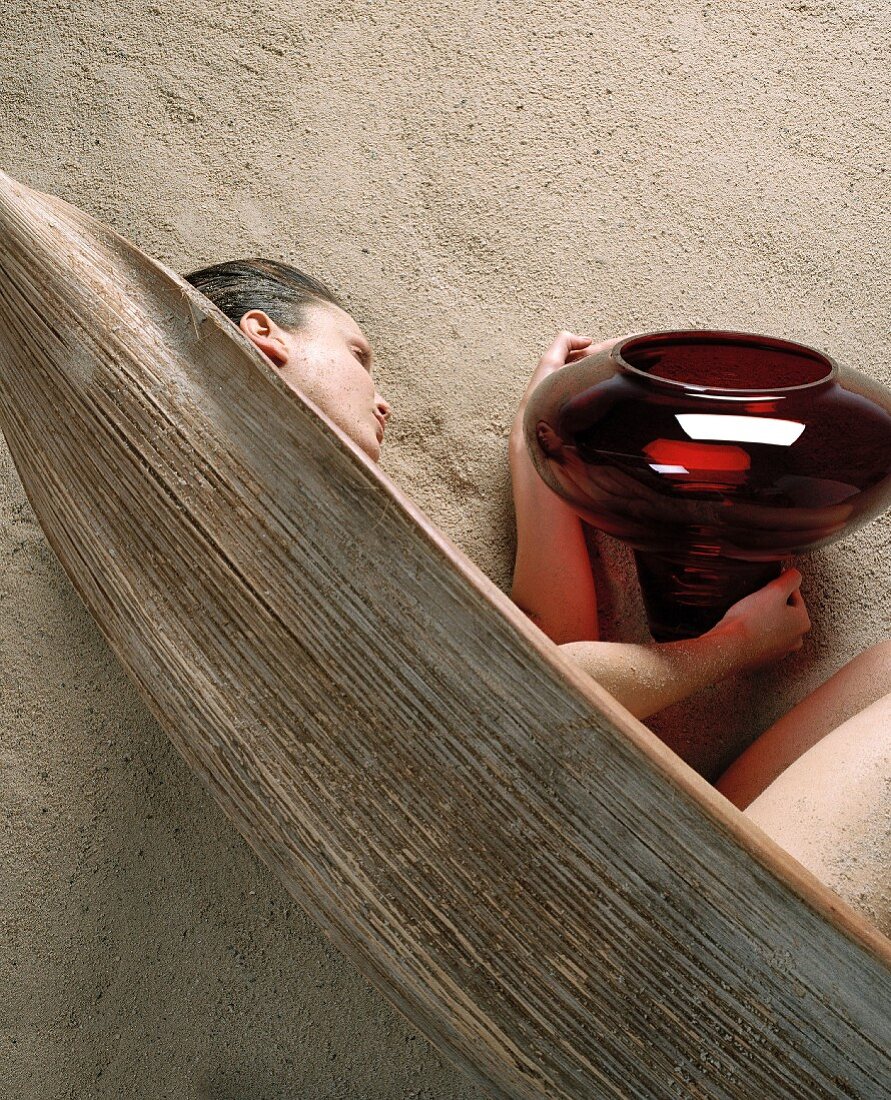 A woman lying on a beach with a weathered canoe and a red glass bowl