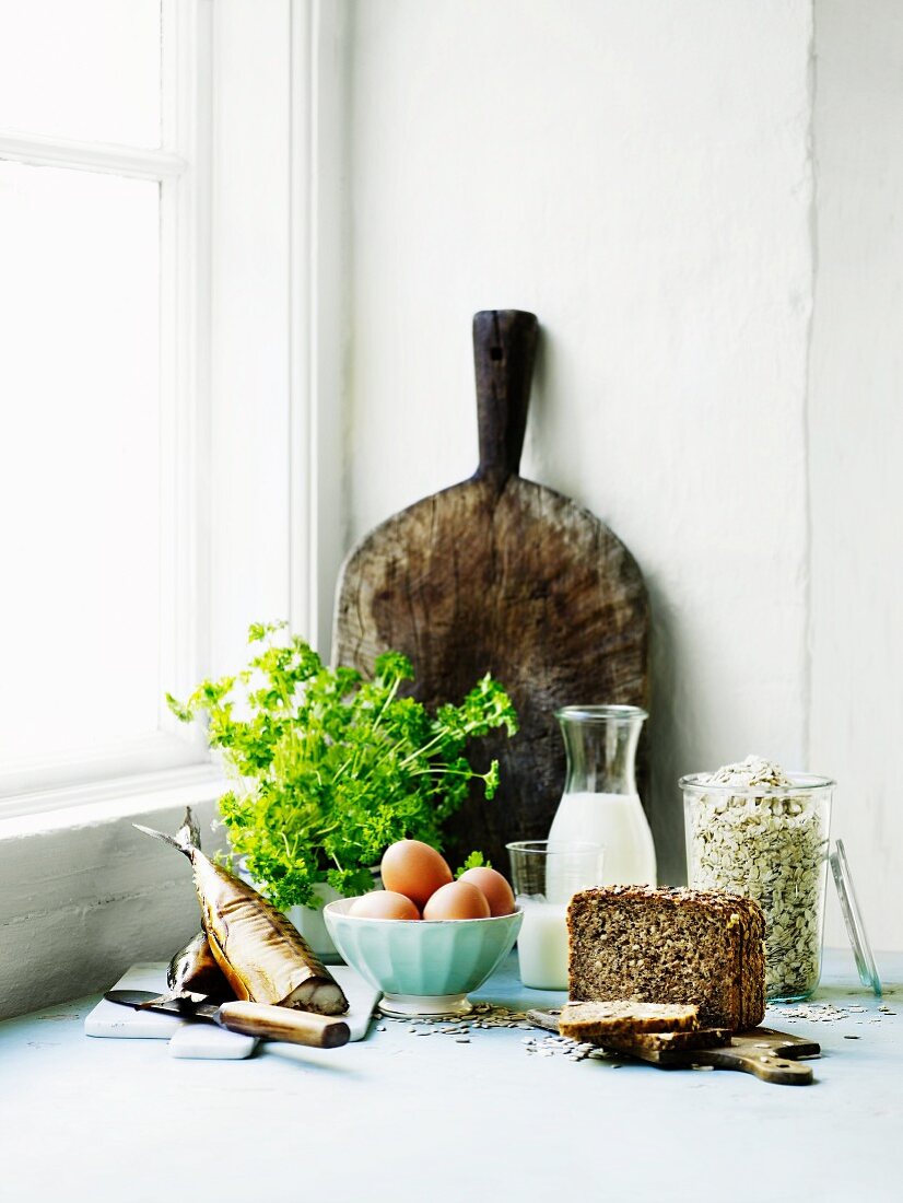 An arrangement of smoked fish, a bunch of parsley, bread and a rustic wooden chopping board