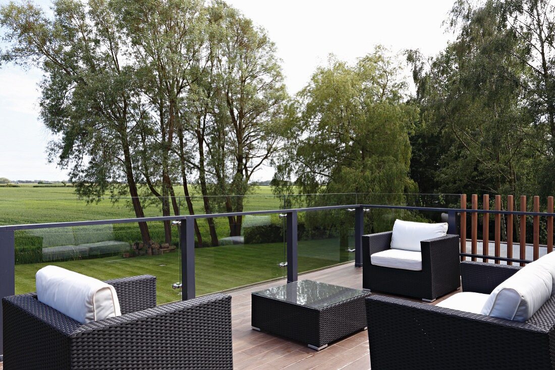 Black rattan outdoor furniture with white cushions on terrace with view across landscape
